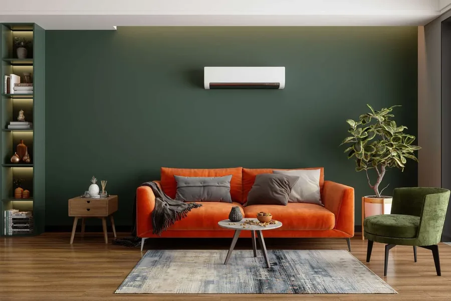 White DIY mini split heat pump indoor unit mounted high on a dark green living room wall above an orange sofa