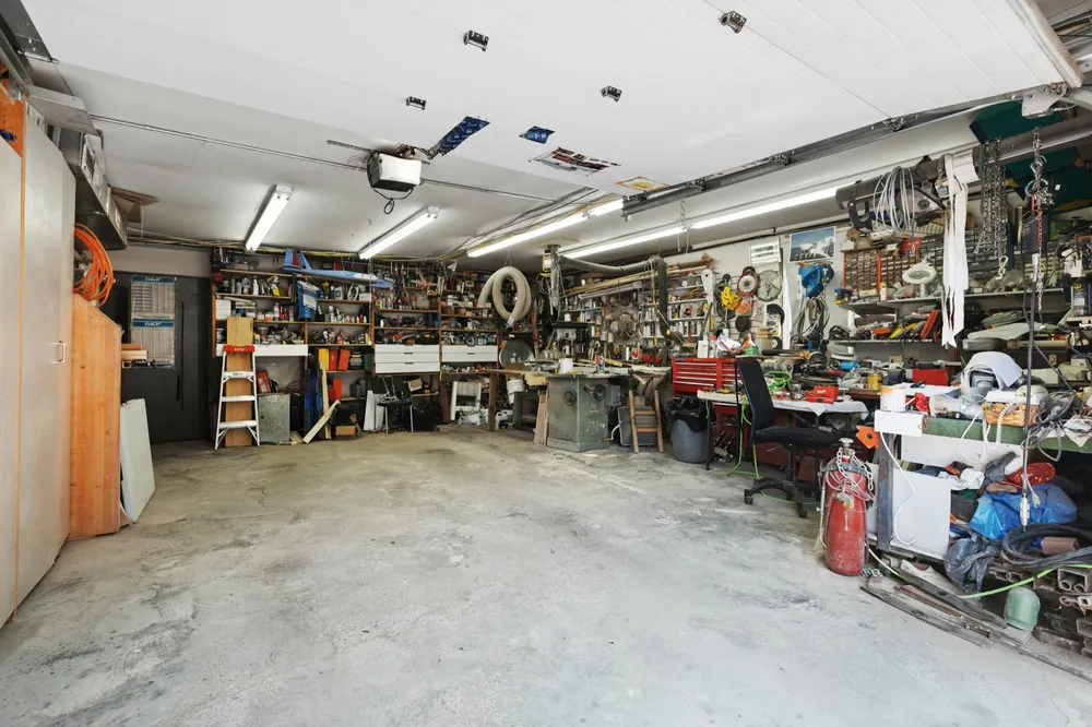 Cluttered garage workshop with tools and workbenches, featuring a mini split for garage best mounted on the left wall